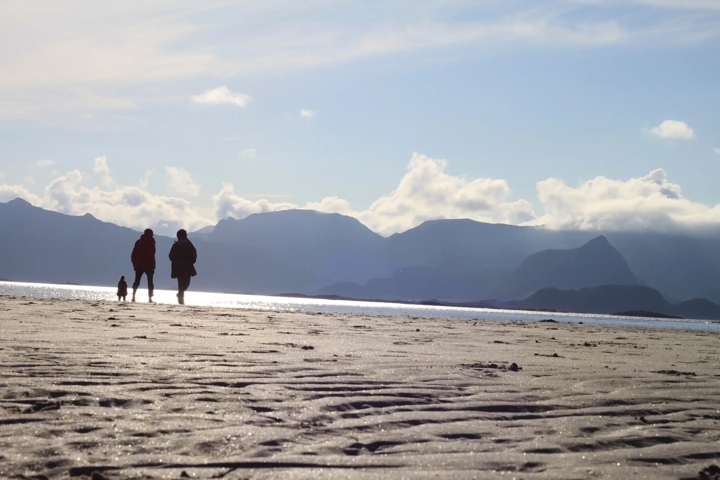 To voksne og et barn som går på en strand.